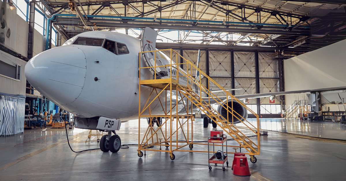 zdjęcie przedstawiające hangar oraz samolot poddawany naprawie z dostawionymi do niego schodkami dla technika
